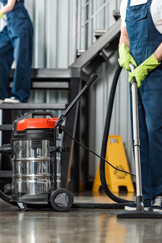 cropped view of cleaner vacuuming floor near colleague cleaning stairs